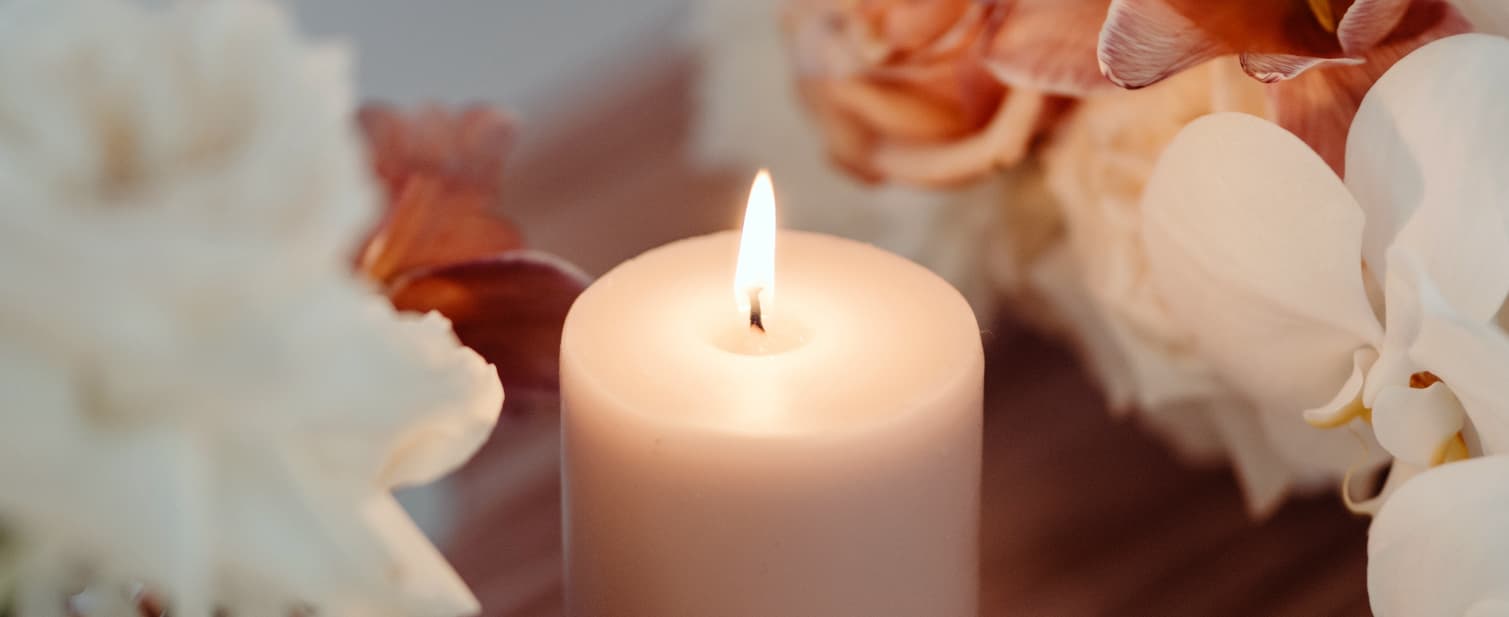 Close-up of a lit candle surrounded by soft floral decorations creating a warm, calming atmosphere